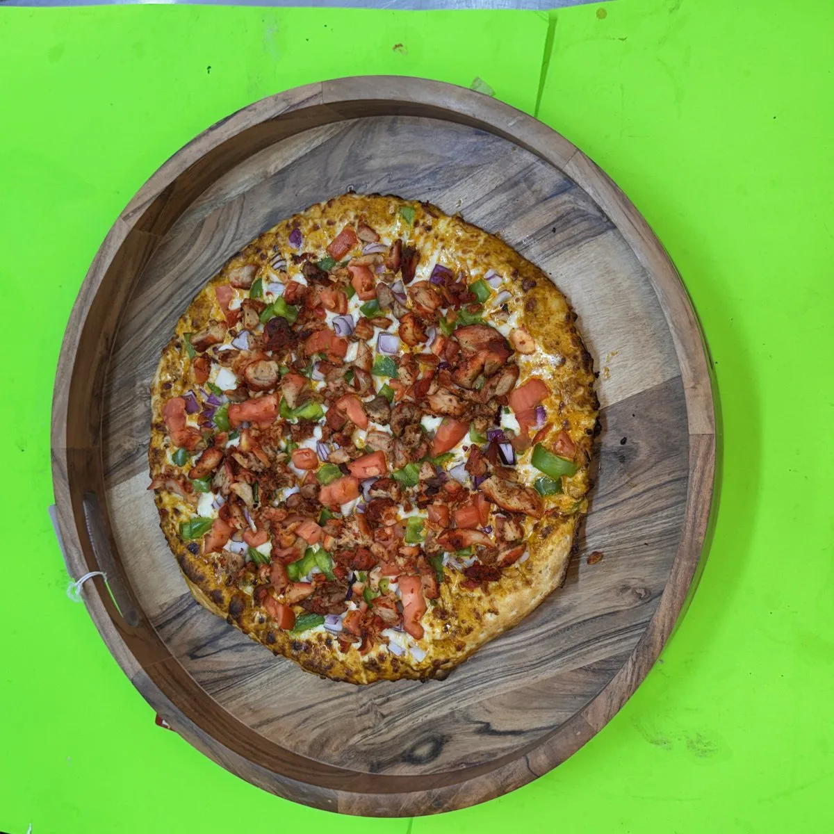 Tandoori Chicken pizza on wooden board, topped with spiced chicken, tomatoes, onions, cilantro. 100% halal, cooked to order on Valley Street, Providence